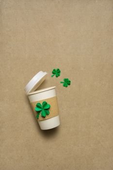 Creative St. Patricks Day concept photo of take away coffee cup with shamrocks made of paper on brown background.
