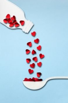 Creative valentines concept photo of bottle and spoon made of paper with hearts on blue background.