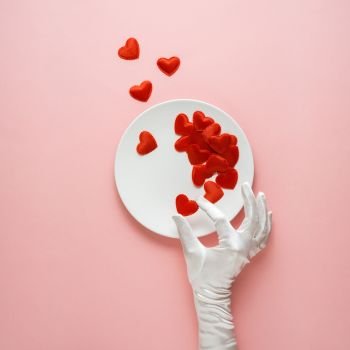 Creative concept photo of kitchenware with hand, painted plate with food on it on pink background.