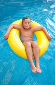 Blond kid floating in the swimming pool. Blond kid floating on a yellow inflatable in the swimming pool