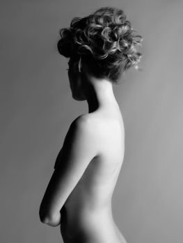Black and white portrait of sensual nude woman with elegant hairstyle on gray background