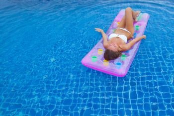 Woman in bikini in swimming pool. Woman in bikini floating on inflatable mattress in swimming pool