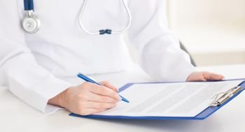 Doctor writing on sheet in clipboard. Female doctor hands writing on sheet in a clipboard with a pen