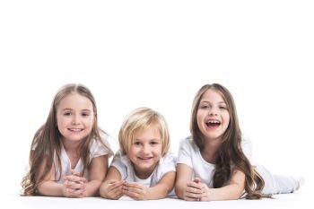 Happy children isolated on white. Happy smiling three children in white clothes laying on floor isolated on white background