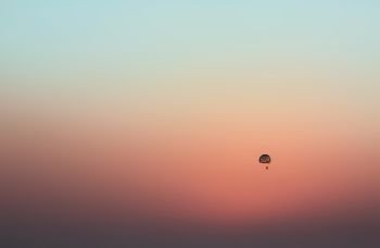 The distant parachute flies across the sky at dusk