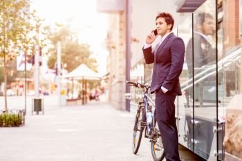Successful businessman with bicycle. Successful businessman in suit with bicycle in city talking over mobile phone