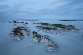 Beautiful long exposure landscape image of low tide beach with rocks at sunrise