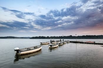 UK. Summer sunset landscape image over calm lake with leisure boats on jetty