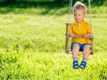 Portrait of toddler child swinging outdoors. Rural scene with one year old baby boy at swing. Healthy preschool children summer activity. Kid playing outside. 