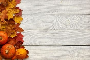 Autumn leaves and pumpkins over old wooden background with copy space