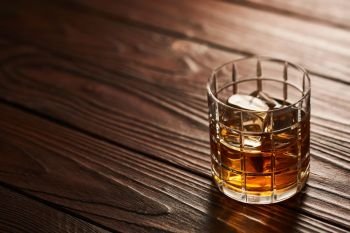 Glass of whiskey with ice cubes on rustic wooden table with copy-space