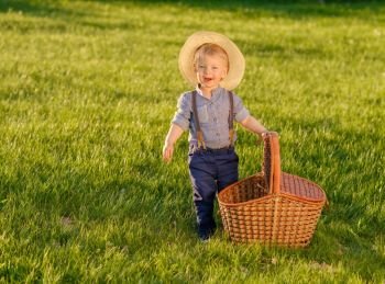 Portrait of toddler child outdoors. Rural scene with one year old baby boy wearing straw hat and picnic basket