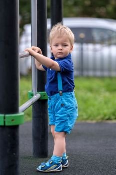 Portrait of toddler child outdoors wearing shorts and suspenders. One year old baby boy at playground