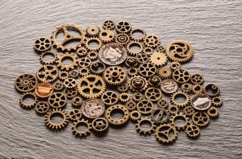 Various metal cogwheels and gear wheels with USA coins over slate background