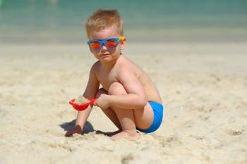 Two year old toddler boy playing with shovel and sand on beach 