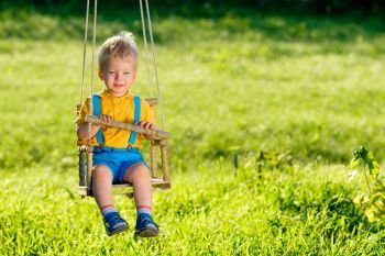 Rural scene with toddler boy swinging outdoors. . Portrait of toddler child swinging outdoors. Rural scene with one year old baby boy at swing. Healthy preschool children summer activity. Kid playing outside. 