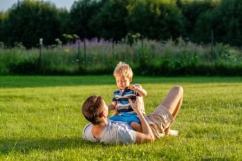 Happy father and son having fun outdoor on meadow. Happy man and child having fun outdoor on meadow.  Family lifestyle scene of father and son resting together on green grass in the park. 
