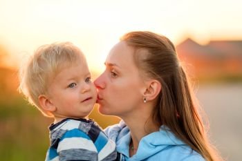 Woman and child outdoors at sunset. Mother kissing her son. . Happy woman and child having fun outdoors.  Family lifestyle rural scene of mother and son in sunset sunlight. Mother kissing her son. 