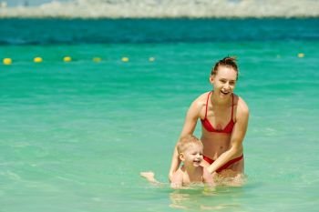 Happy mother teaching her little son to swim. Two year old toddler boy on beach with mother. Happy mother teaching her little son to swim. 