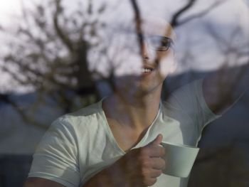 young handsome man drinking morning coffee by the window in his home