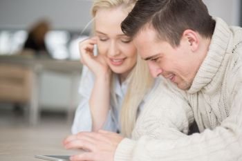 Young Couple on the floor in front of fireplace surfing internet using digital tablet on cold winter day