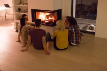 group of young multiethnic couples sitting on the floor in front of fireplace at cold winter night