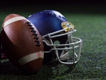 closeup shot of american football and helmet on grass field at night