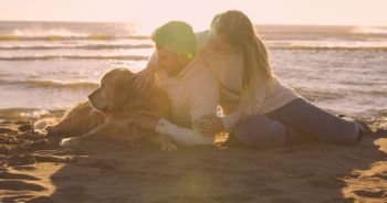 Couple With A Dog enjoying time  together On The Beach at autumn day
