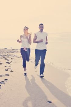 happy young couple running and jogging on beach at early morning