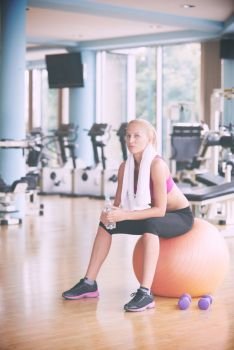 young healthy blonde woman drinking water  in fitness gym while sitting on pilates ball. woman in fitness gym drink water