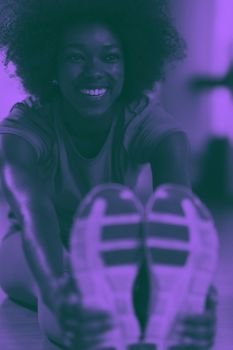 woman in a gym stretching and warming up before workout. happy young african american woman in a gym stretching and warming up before workout duo tone filter