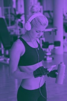 woman with headphones in fitness gym. young healthy woman drinking water  in fitness gym while sitting on pilates ball and listening music on headphones from smartphone duo tone