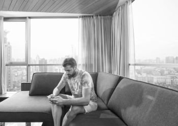 young man sitting on sofa and using a mobile phone  near the window at home. young casual man using a mobile phone at home