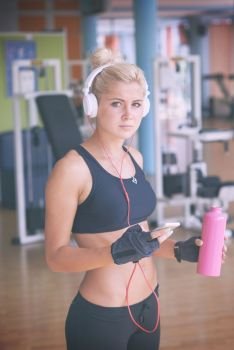 young healthy woman drinking water  in fitness gym while sitting on pilates ball and listening music on headphones from smartphone. woman with headphones in fitness gym