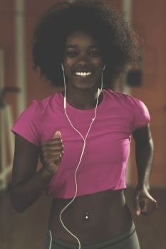 afro american woman running on a treadmill at the gym while listening music on earphones. afro american woman running on a treadmill
