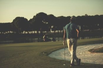 golfer  from back looking to ball and  hole in distance, handsome middle eastern golf player portrait from back with beautiful sunset in background. golfer from back at course looking to hole in distance