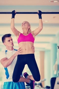 trainer support young woman while lifting on bar in fitness gym indoors. trainer support young woman while lifting on bar in fitness gym