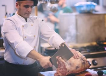 chef using ax while cutting big piece of beef  on wooden board in restaurant kitchen. chef cutting big piece of beef