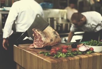 chef using ax while cutting big piece of beef  on wooden board in restaurant kitchen. chef cutting big piece of beef