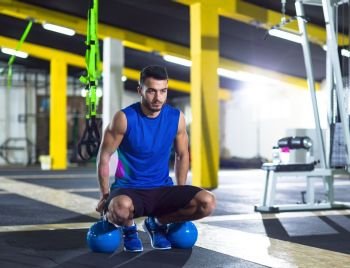Young strong man doing pushups on kettlebells at cross fitness gym. Young strong man doing pushups