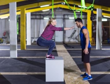 young athletic woman training with personal trainer  jumping on fit box at crossfitness gym. woman working out with personal trainer jumping on fit box
