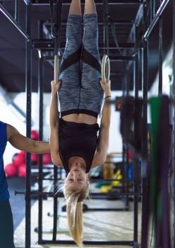 young athletic woman working out with personal trainer on gymnastic rings at the crossfitness gym. woman working out with personal trainer on gymnastic rings