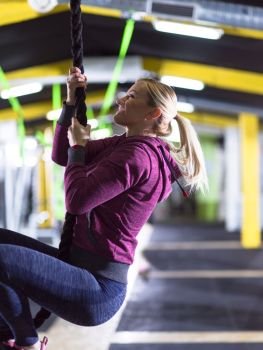 young muscular woman doing rope climbing in crossfitness gym. woman doing rope climbing