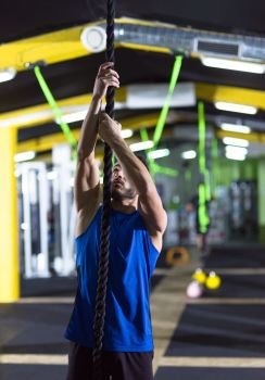 young muscular man doing rope climbing in crossfitness gym. man doing rope climbing