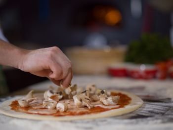 chef putting fresh mushrooms over pizza dough on kitchen table. chef putting fresh mushrooms on pizza dough