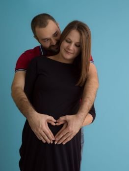 Portrait of a happy young couple,man holding his pregnant wife belly isolated over blue background. pregnant couple  isolated over blue background