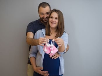 young  pregnant couple holding newborn baby shoes isolated on white background in family and parenthood concept. pregnant couple holding newborn baby shoes