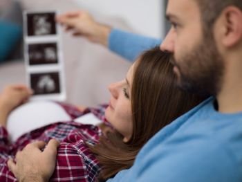 pregnant couple looking baby’s ultrasound. Young pregnant couple looking baby’s ultrasound photo while relaxing on sofa at home
