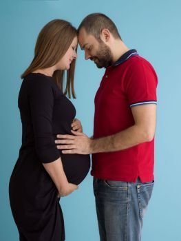 pregnant couple  isolated over blue background. Portrait of a happy young couple,man holding his pregnant wife belly isolated over blue background