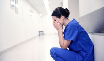 people, medicine, healthcare and sorrow concept - sad or crying female nurse at hospital corridor. sad or crying female nurse at hospital corridor